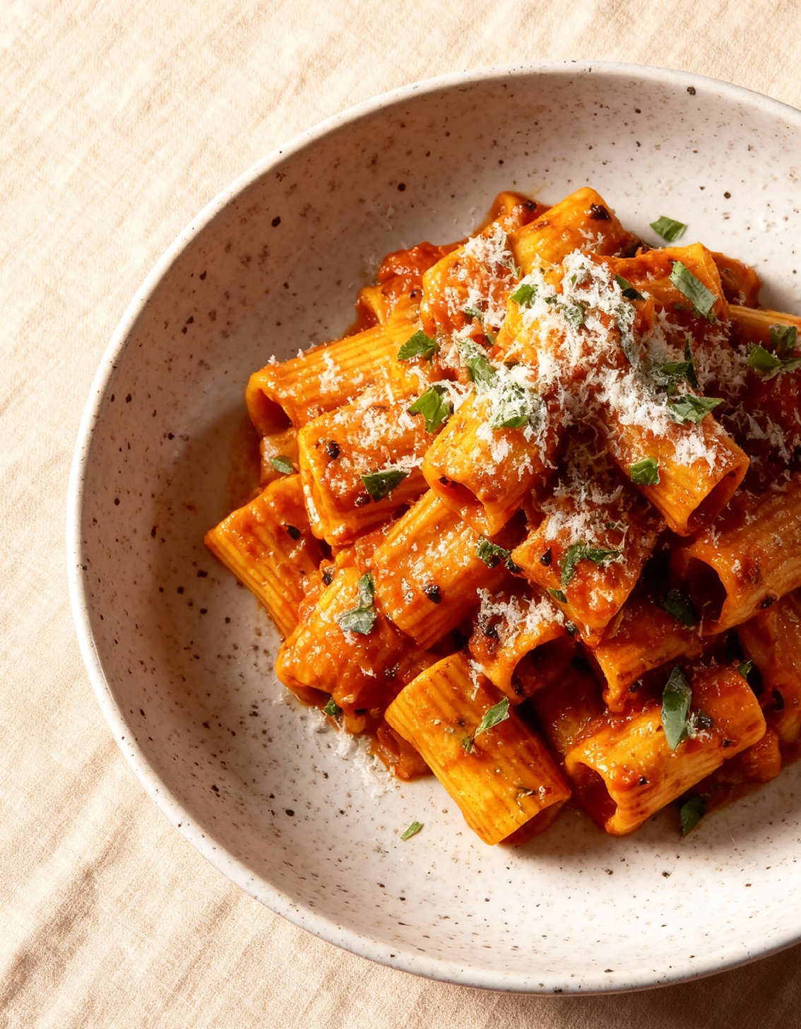 Een kom met rigatoni pasta bedekt met tomatensaus, geraspte kaas en verse kruiden.