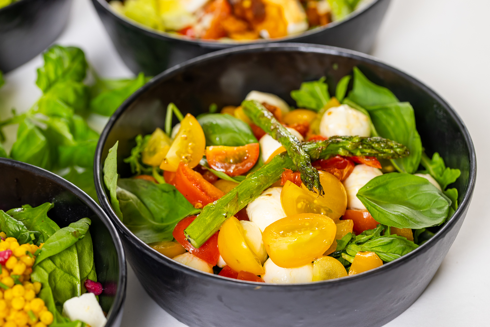 Saladeschaal met gele en rode kerstomaten, mozzarella, groene asperges en verse basilicumblaadjes.