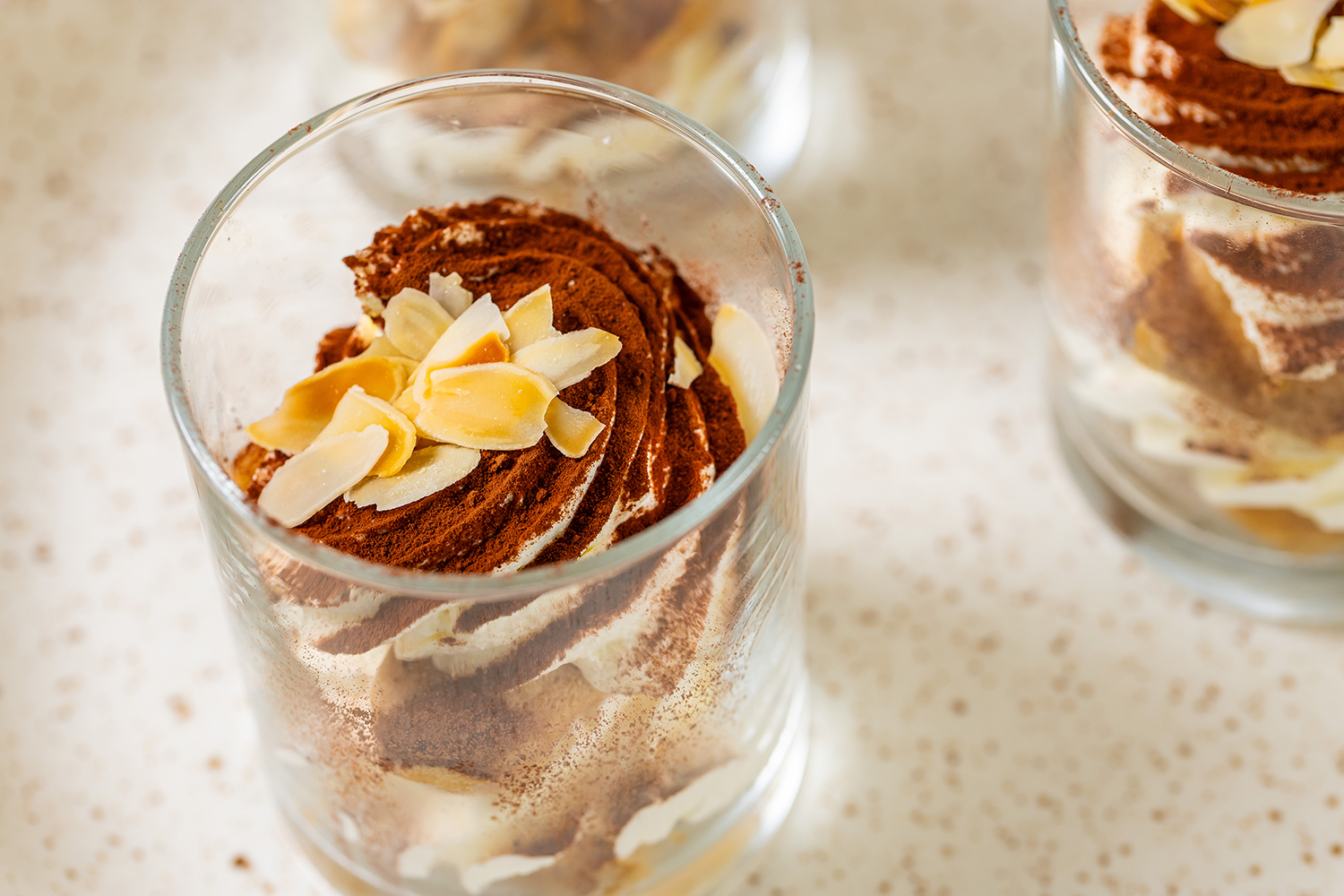 Glas tiramisu dessert met cacaopoeder en amandelschaafsel erop.