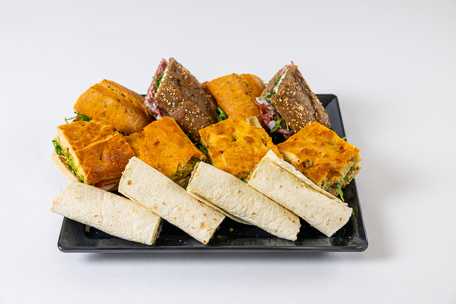 Een bord met diverse sandwiches en wraps met verschillende broodsoorten en vullingen, geplaatst op een witte achtergrond.