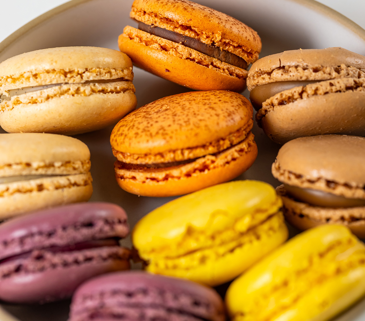 Een plaat met verschillende gekleurde macarons in geel, oranje, paars en beige tinten.