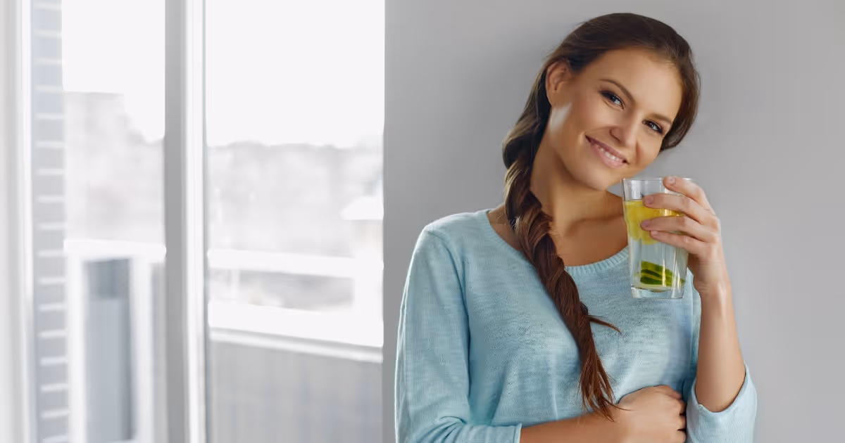 Smiling woman in blue sweater drinking green beverage near window