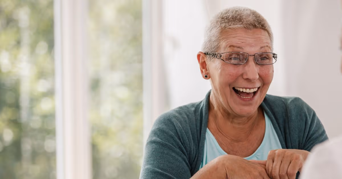 Older woman laughing joyfully by window in green cardigan