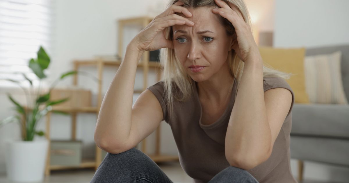 Distressed woman holding head, looking worried in a living room