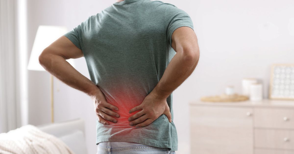 Person experiencing lower back pain, hands on painful red area