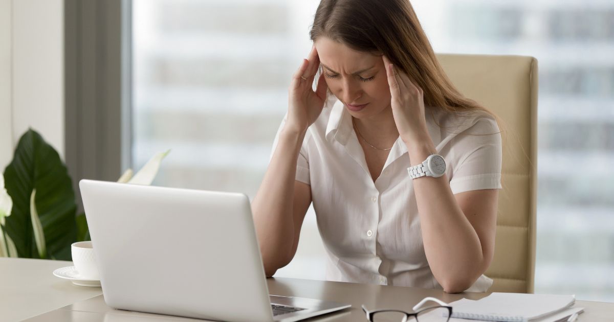 Stressed woman with headache working on laptop in office