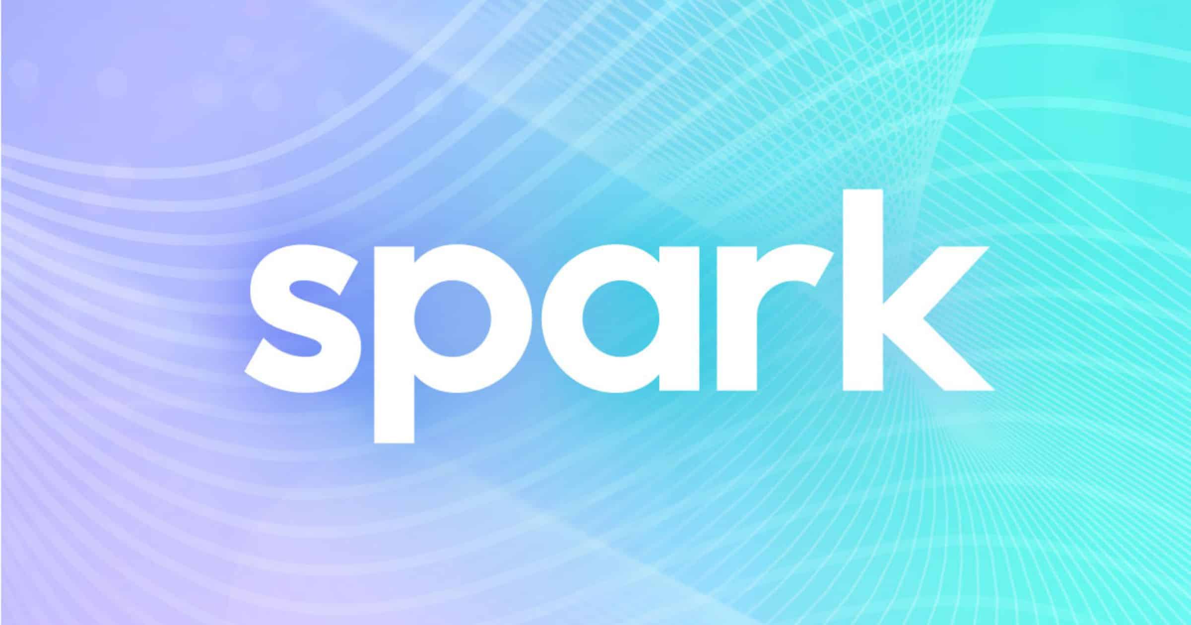 Close-up photo of a stylised orange spark graphic on a white background, with a bright light burst at the centre and subtle texture around the edges.