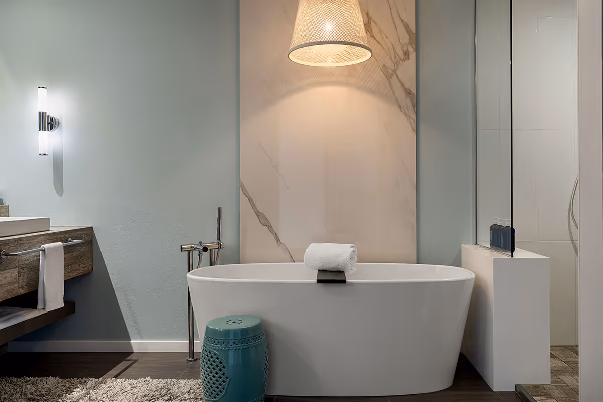 Modern bathroom with a white freestanding tub, rolled towel, pendant light, vanity, and glass shower enclosure.