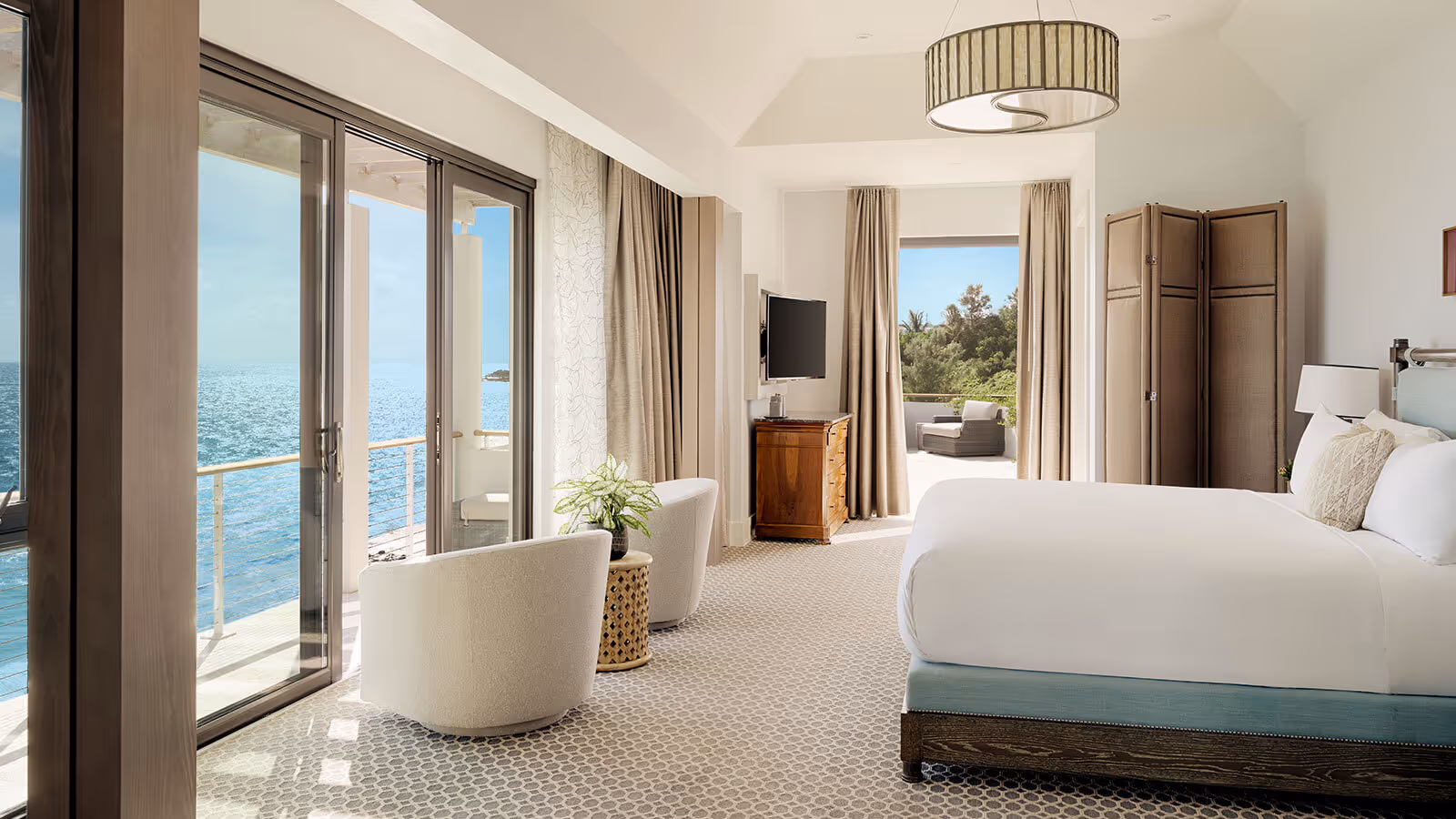 Spacious bedroom with large windows, ocean view, seating area, TV, and neutral-toned furnishings.