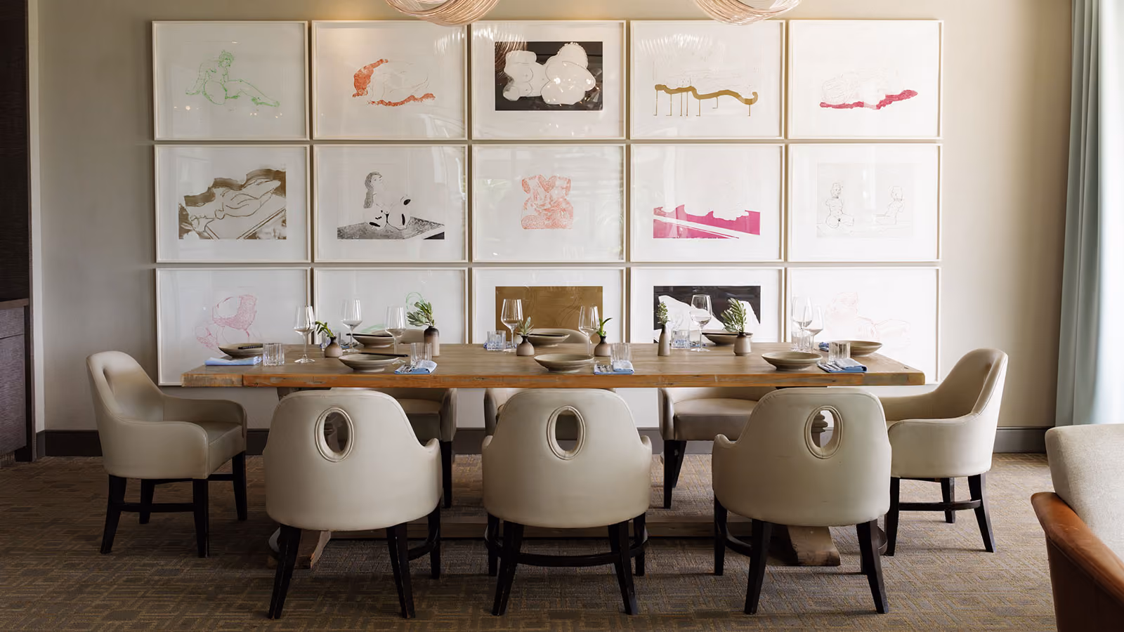 Dining room with wooden table, eight beige chairs, table set with dishes, glasses, and small vases.