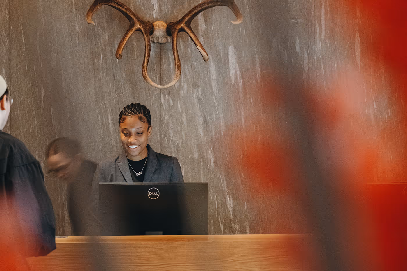 A receptionist smiles behind a desk with a Dell monitor; antlers are mounted on the wall above her.