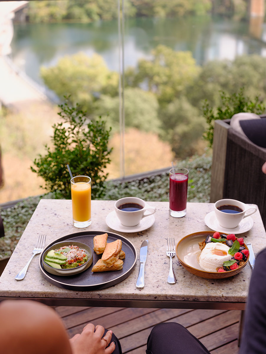 Two people sit at a table with coffee, juice, potato wedges, avocado toast, and a dessert topped with berries.