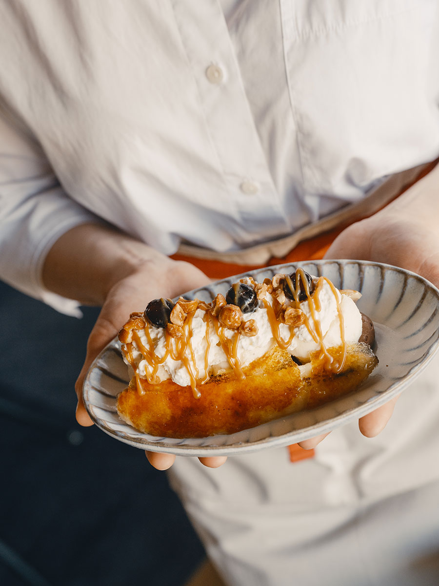 Person holding a plate with cake topped with whipped cream, caramel sauce, and berries.