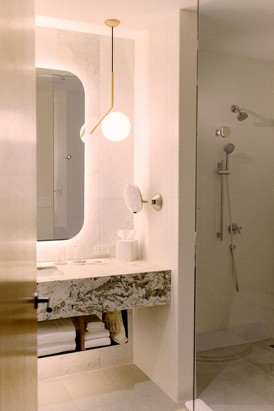 Modern bathroom with marble sink, large mirror, towel storage, and a glass-enclosed shower with handheld and wall-mounted fixtures.