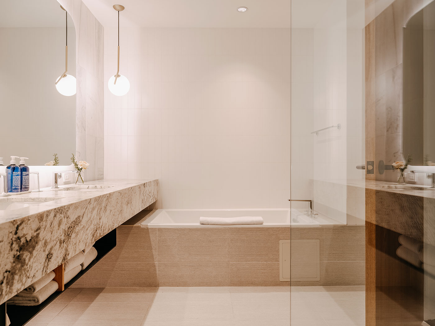 Modern bathroom with a marble countertop, double sink, built-in bathtub, and two hanging pendant lights.