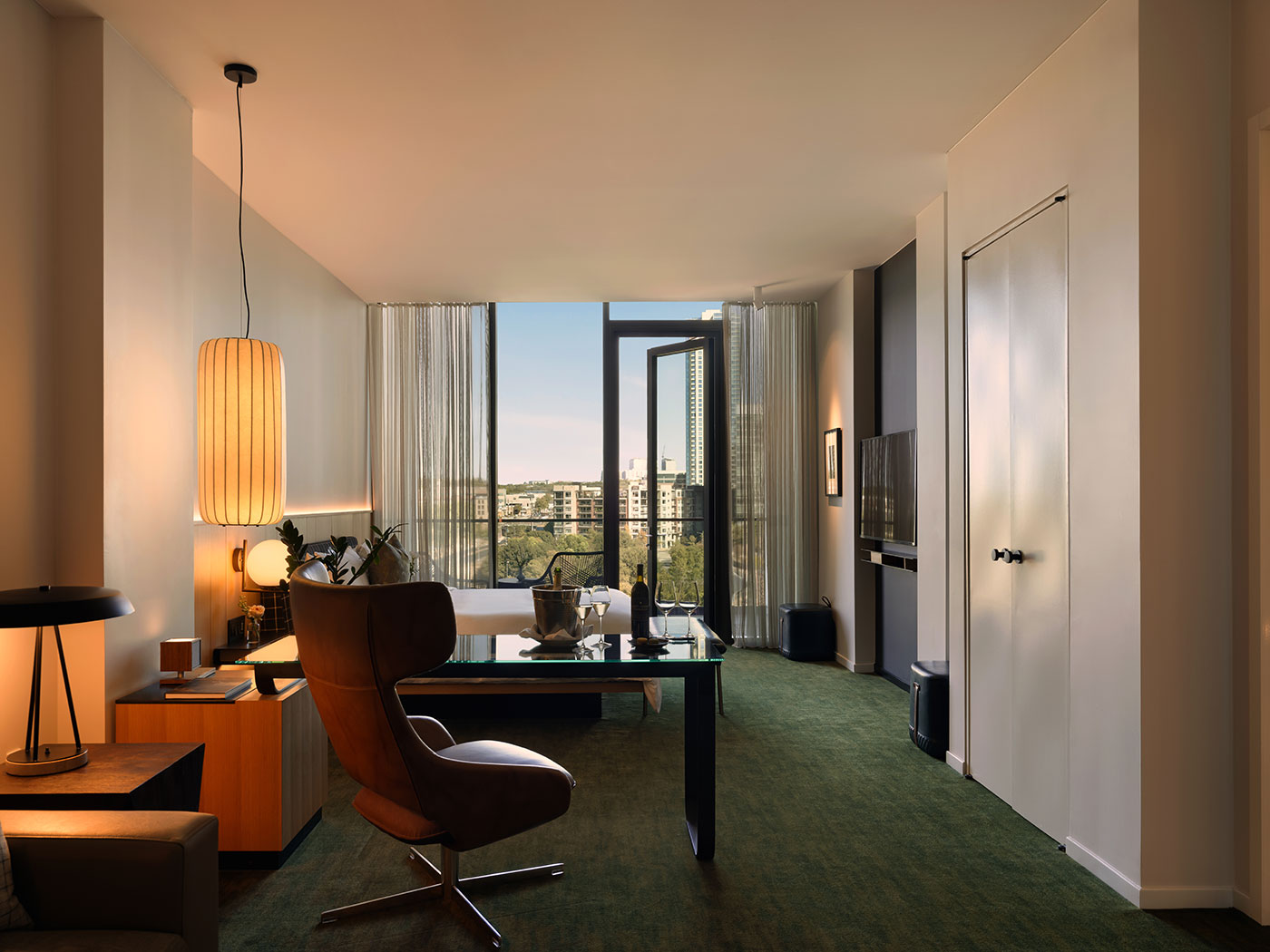 Modern home office with a desk, chair, sofa, large window, and city view through an open glass door.
