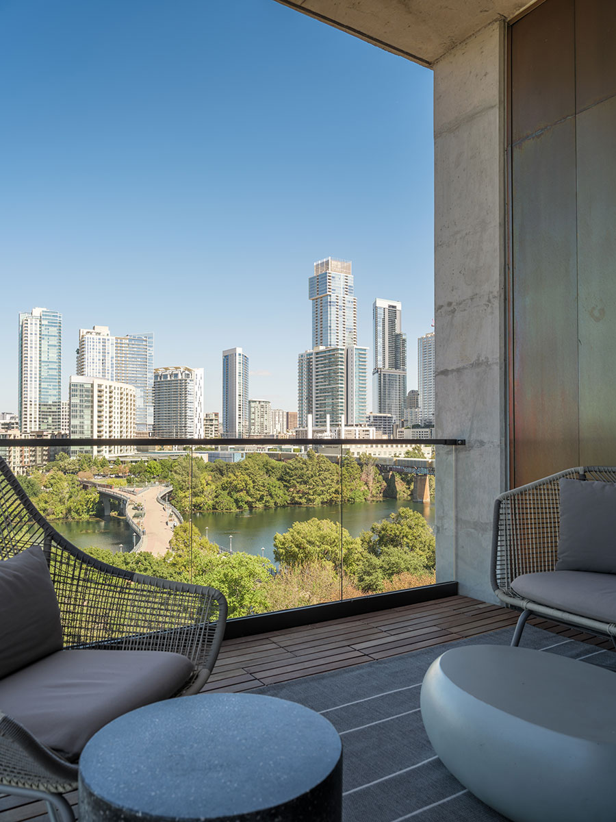 Modern balcony with outdoor seating overlooks a river and city skyline under a clear blue sky.