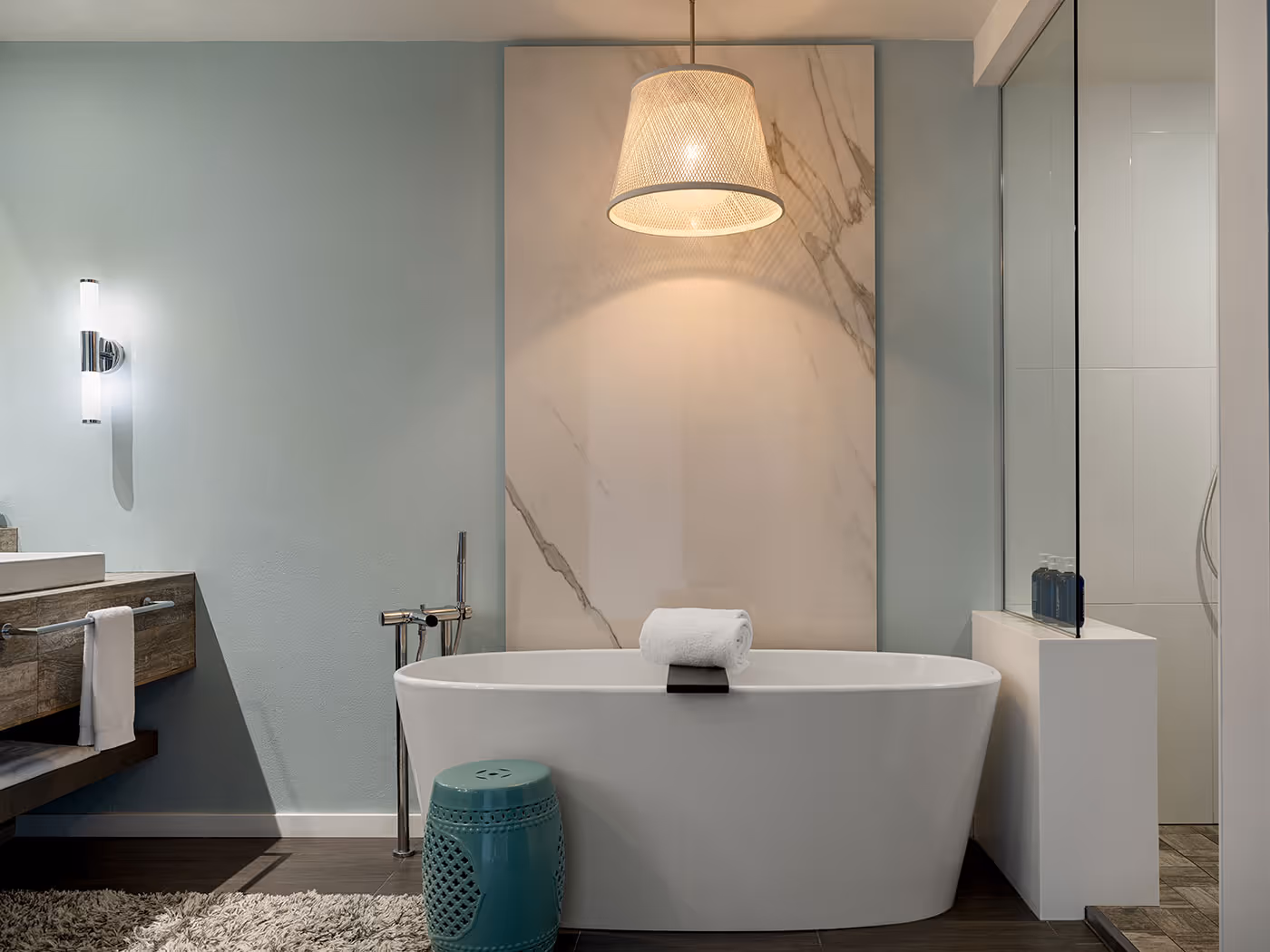 Modern bathroom with a freestanding tub, overhead pendant light, and towel on the tub, featuring minimalist decor.