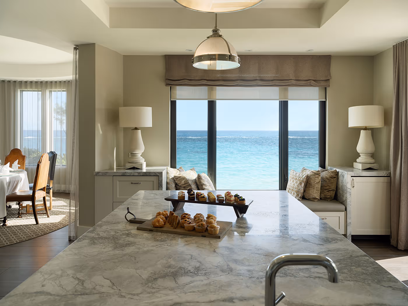 Modern kitchen island with pastries, overlooking a seating area and large windows with an ocean view in the background.