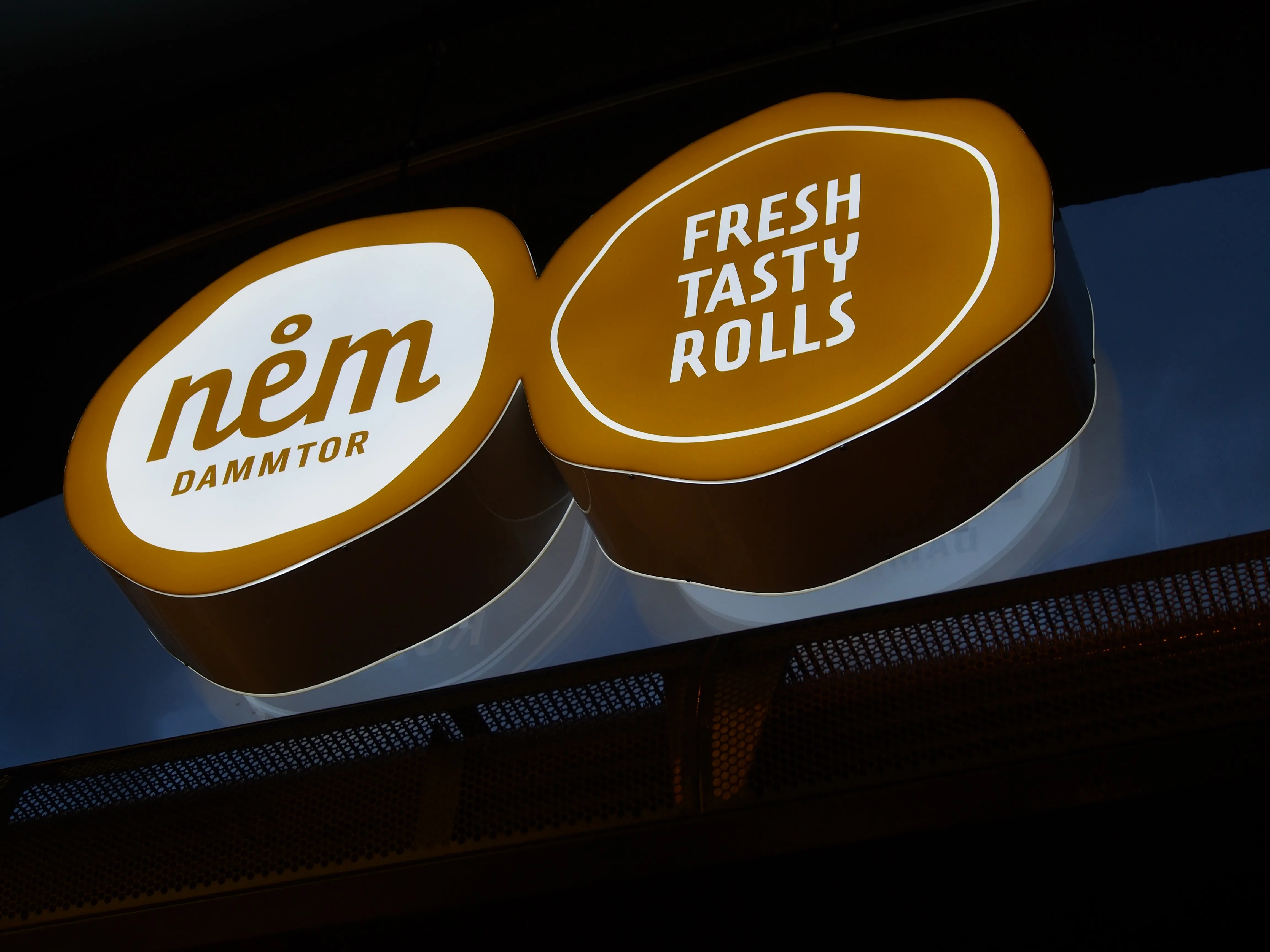 Leuchtschild mit dem Text „nēm DAMMTOR“ und „FRESH TASTY ROLLS“ vor dunklem Hintergrund.