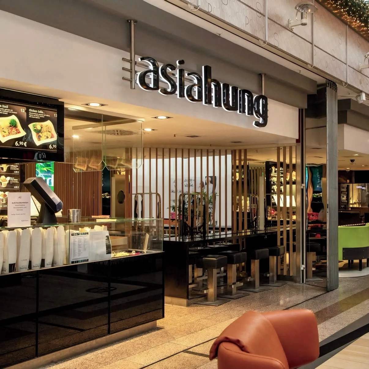 Eingangsbereich eines modernen Asia-Imbiss mit schwarzer Theke, Barhockern und beleuchtetem Schriftzug "Asia Hung".
