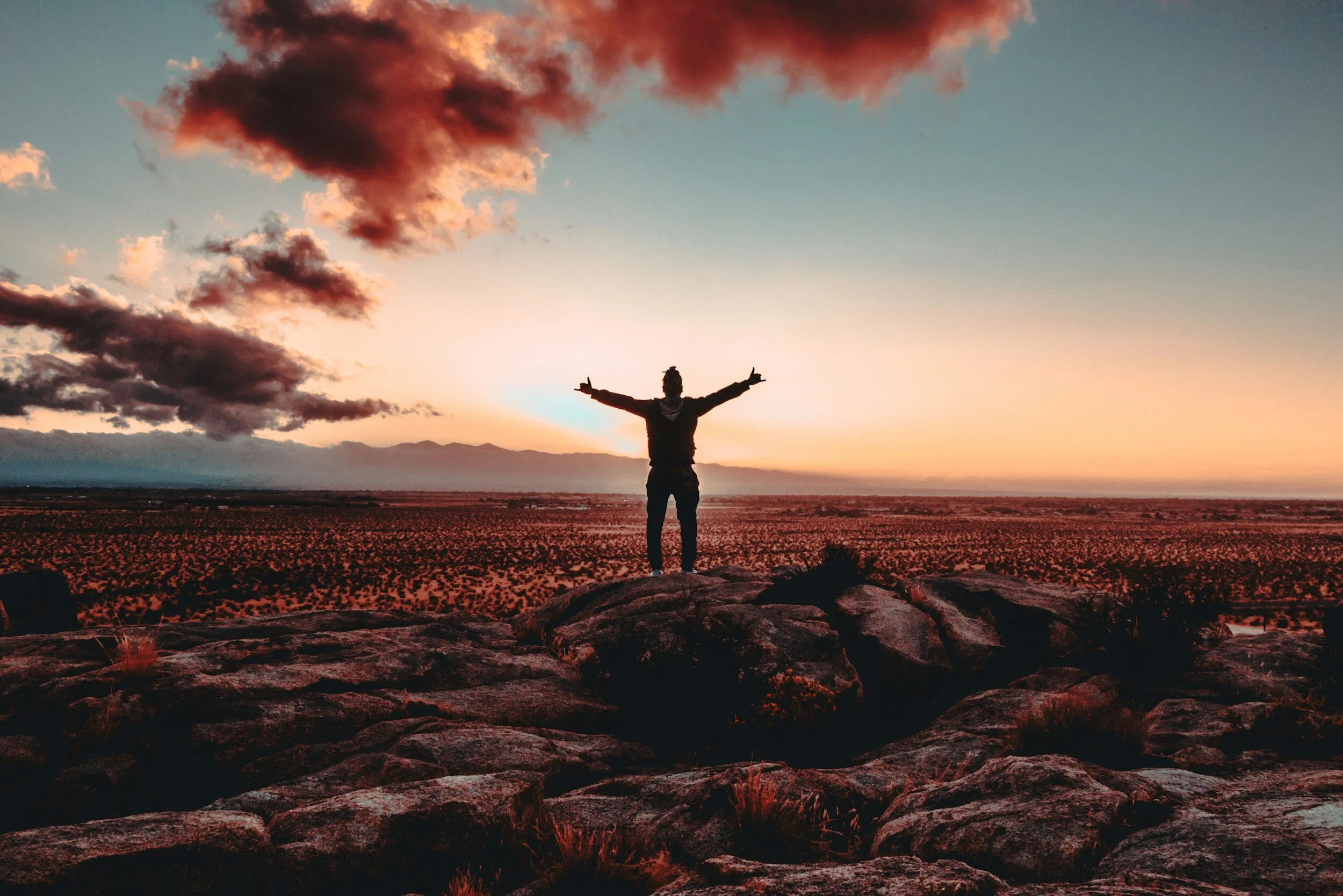 a person standing on a rocky hill with their arms raised