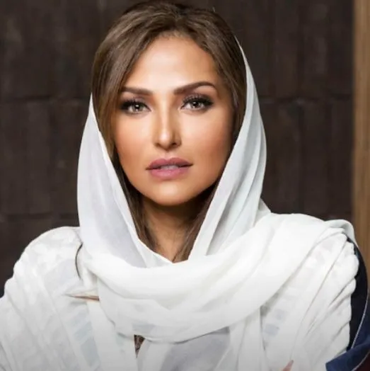 Portrait of a woman with light brown hair wearing a white headscarf and shawl, looking directly at the camera.