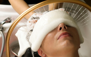 A woman with a warm towel covering her eyes having her head washed.