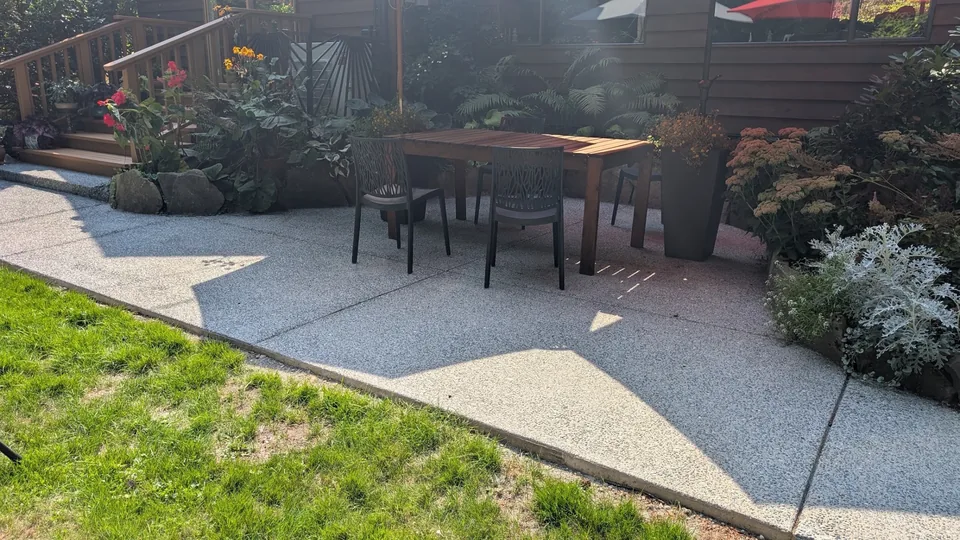 Concrete patio with outdoor dining furniture beside garden beds.