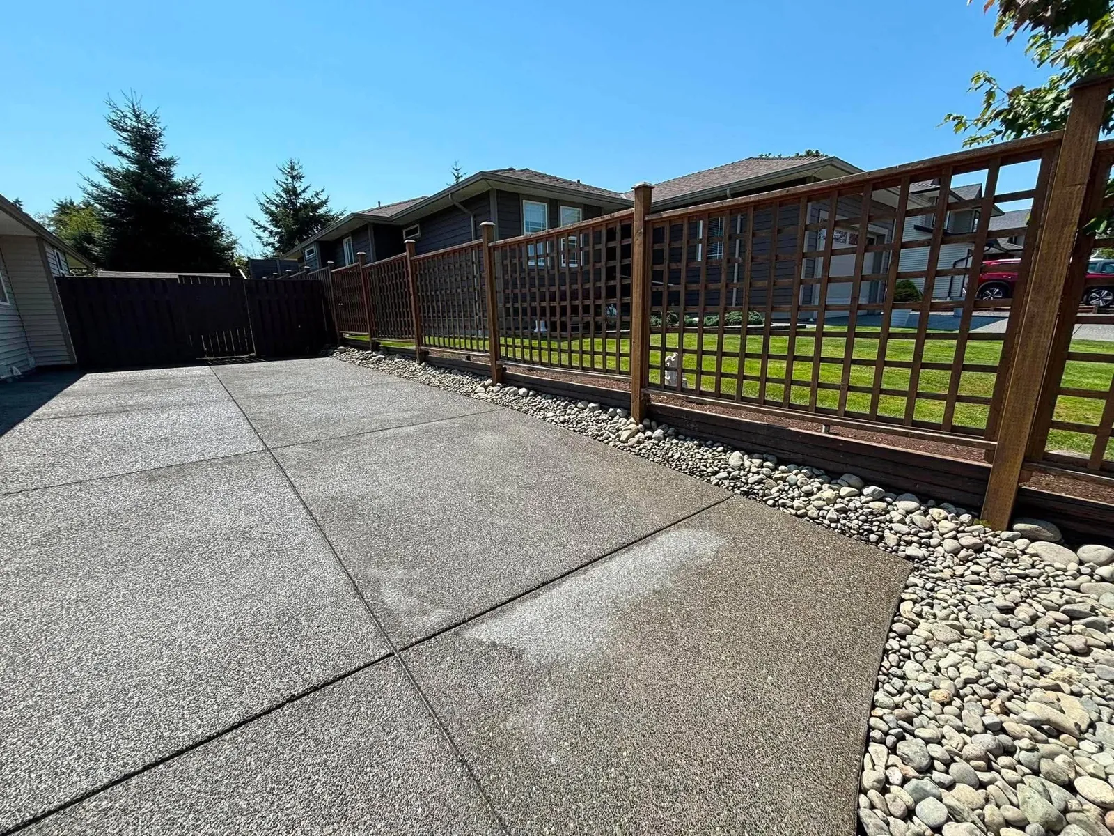 Concrete surface with control joints beside a wood lattice fence and river-rock border.