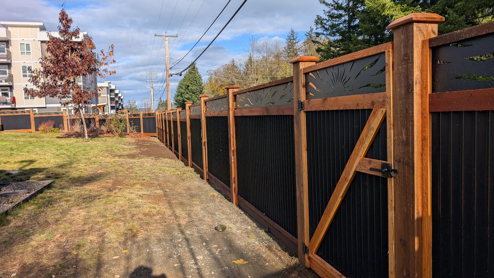Wood-framed black-panel fence and gate with decorative upper panels.