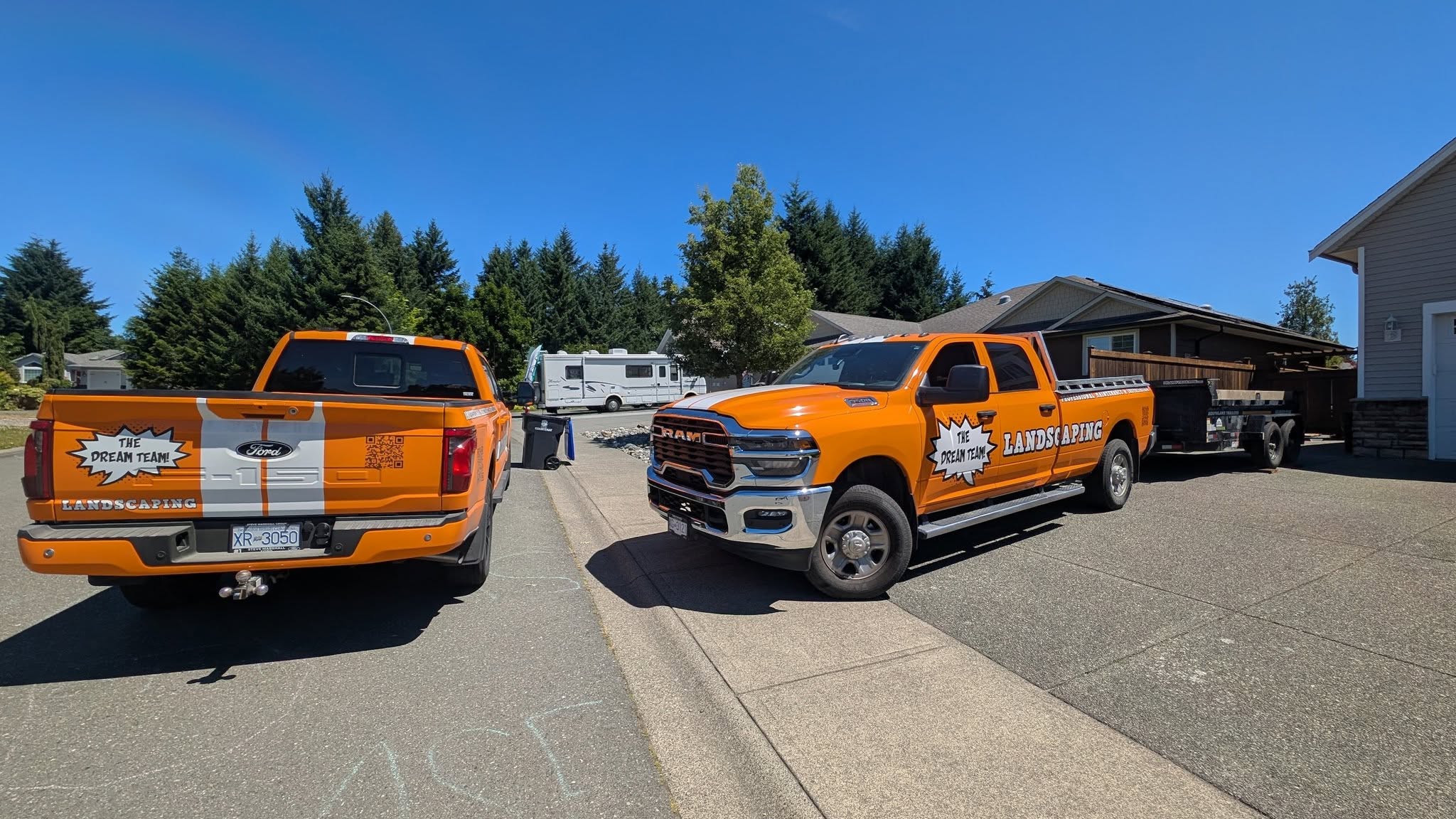 Two orange Dream Team Landscaping trucks with visible company logos and a work trailer.