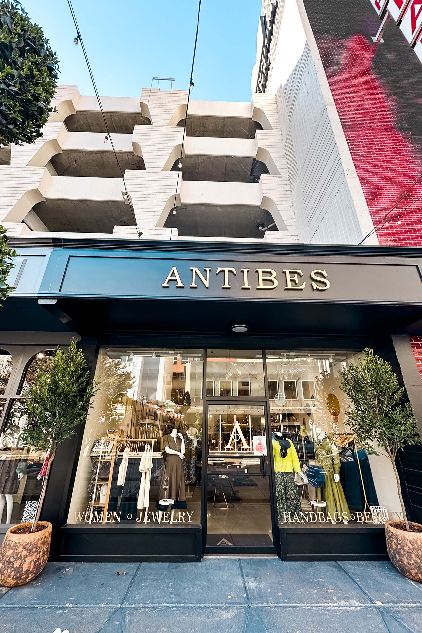 “Street view of Furnish storefront with large windows, black exterior, and signage reading ‘Home, Lifestyle, Gift,’ surrounded by plants and city buildings.”