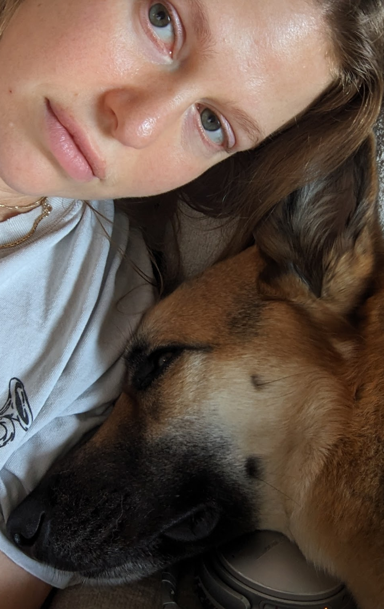 Close-up of a woman with fair skin and light eyes lying down next to a resting German Shepherd dog.