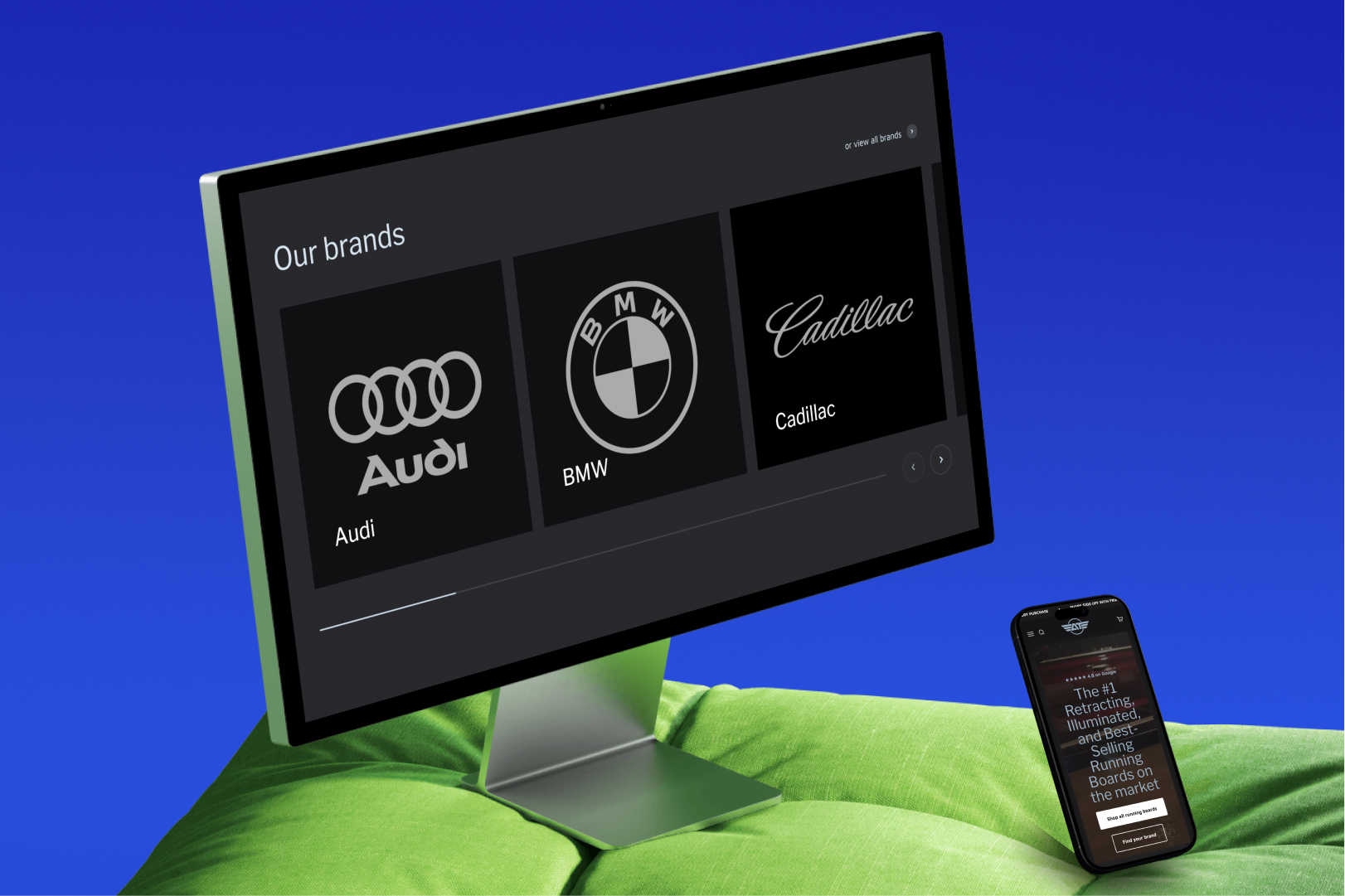 Desktop monitor showing car brand logos Audi, BMW, and Cadillac, with a smartphone displaying a product page on a green fabric surface against a blue background.