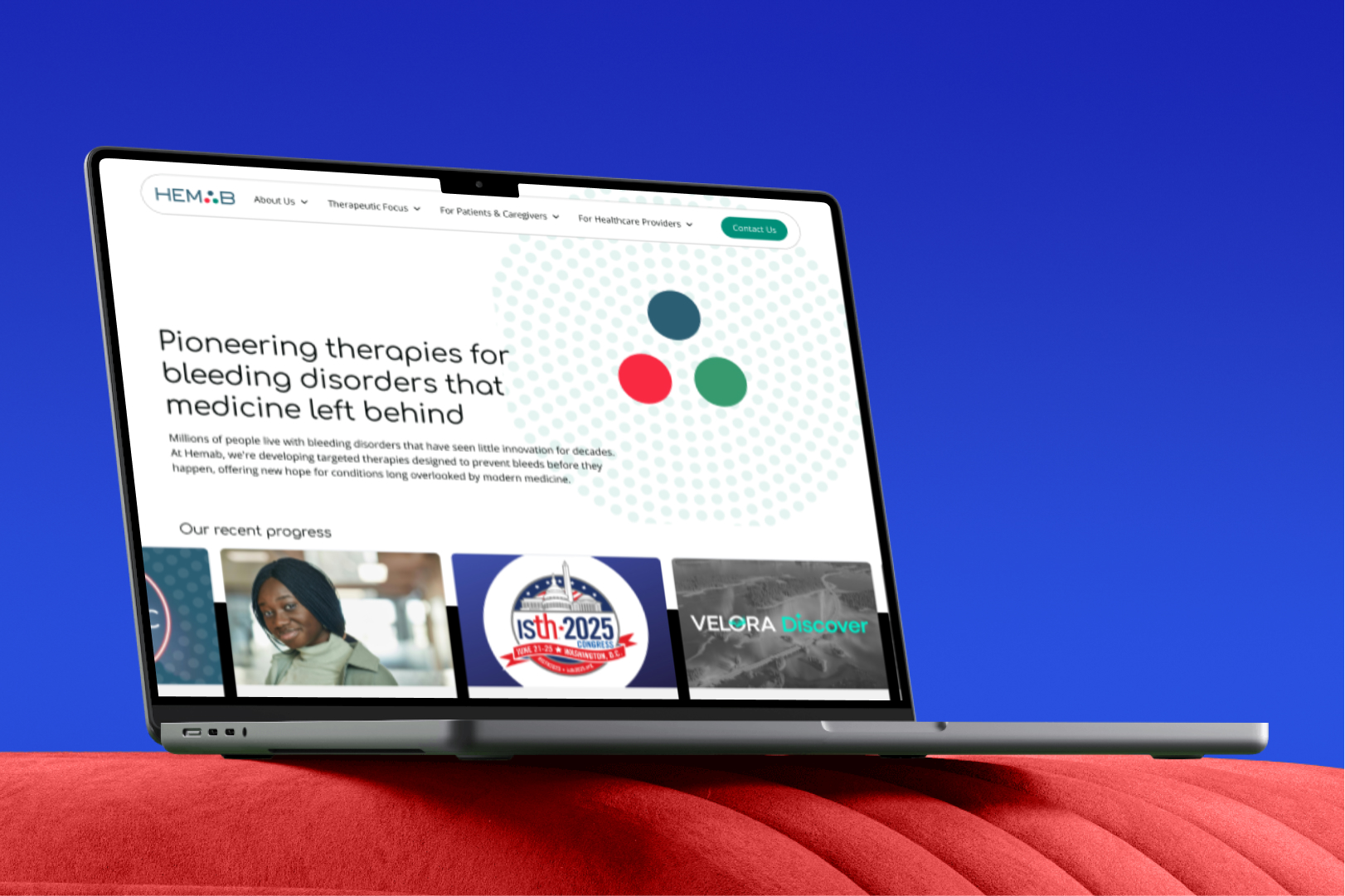 Laptop on red surface showing Hemab website with text about pioneering therapies for bleeding disorders and recent progress highlights.