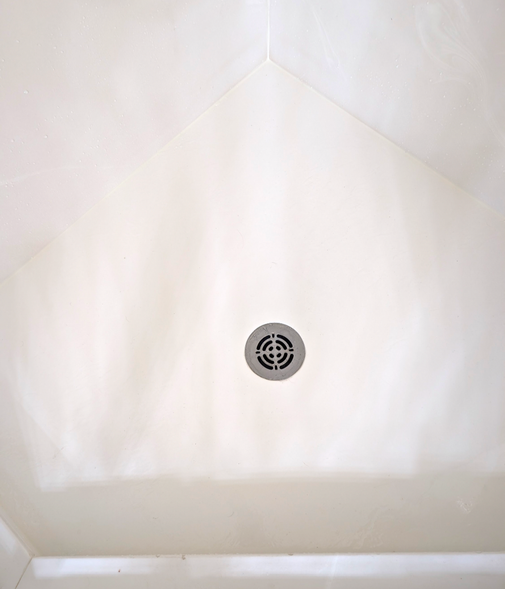 Close-up of a clean white shower floor with a round metal drain in the center.