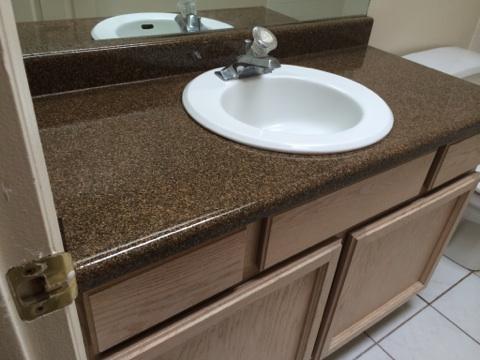 Bathroom vanity with a brown granite countertop, white oval sink, and a silver faucet.