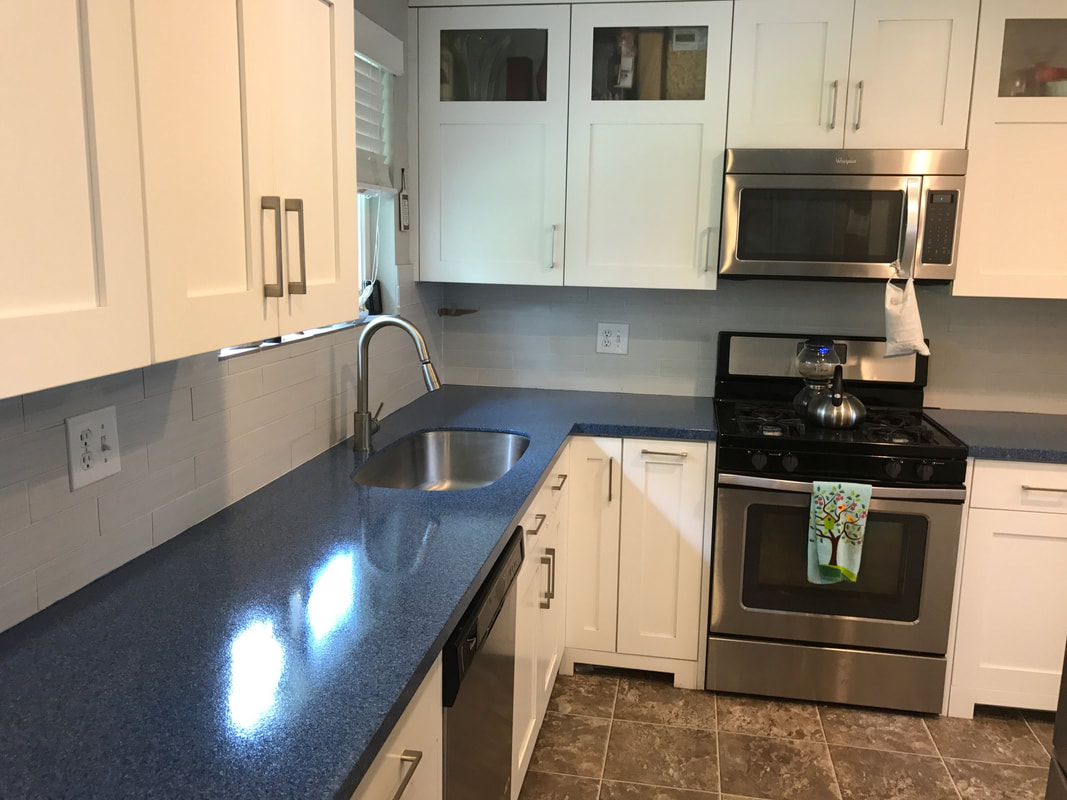 Modern kitchen with white cabinets, blue countertops, stainless steel sink and dishwasher, gas stove with kettle, and microwave above.