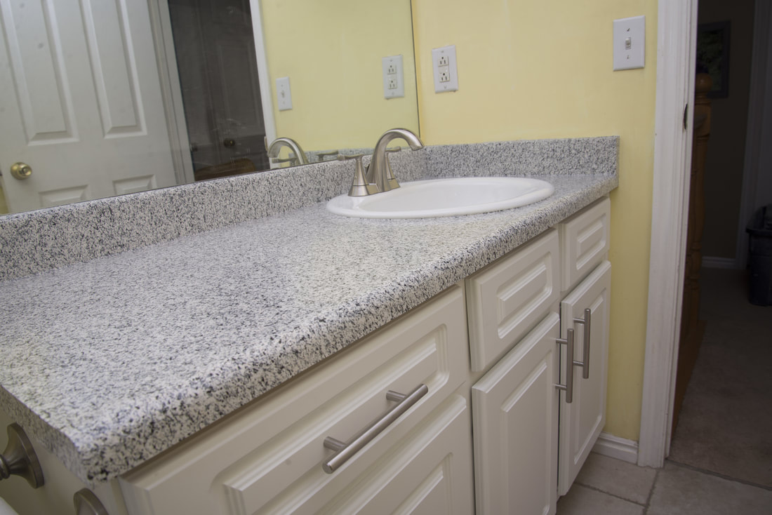 Bathroom sink with a speckled granite countertop and white cabinets under a large mirror.