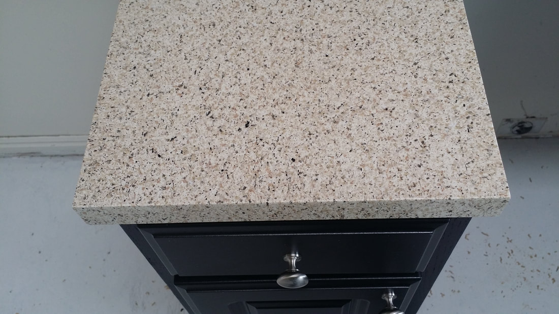 Beige granite countertop with black speckles on a black cabinet with silver handles.
