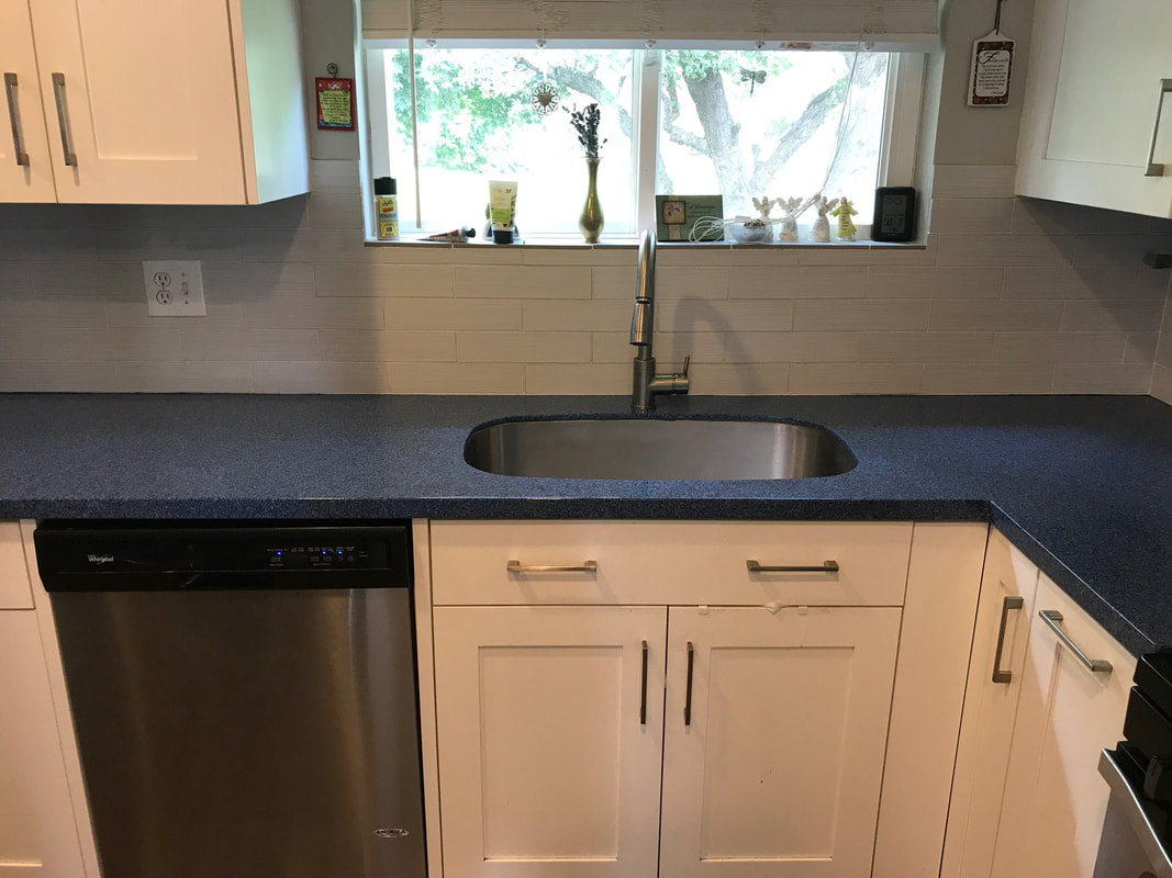 Modern kitchen sink with stainless steel faucet, dark blue countertop, white cabinets, and a dishwasher under the counter next to the sink.