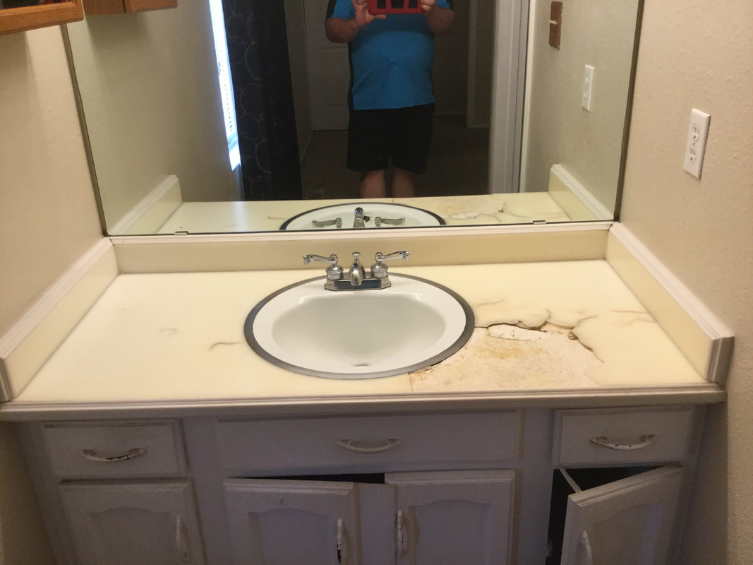Bathroom sink with a cracked and stained countertop and partially open cabinet doors below.