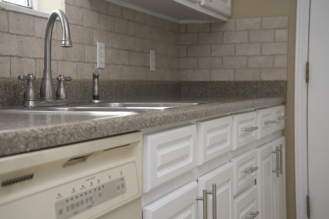 Kitchen countertop with a double stainless steel sink, a curved faucet, and white cabinets with silver handles.
