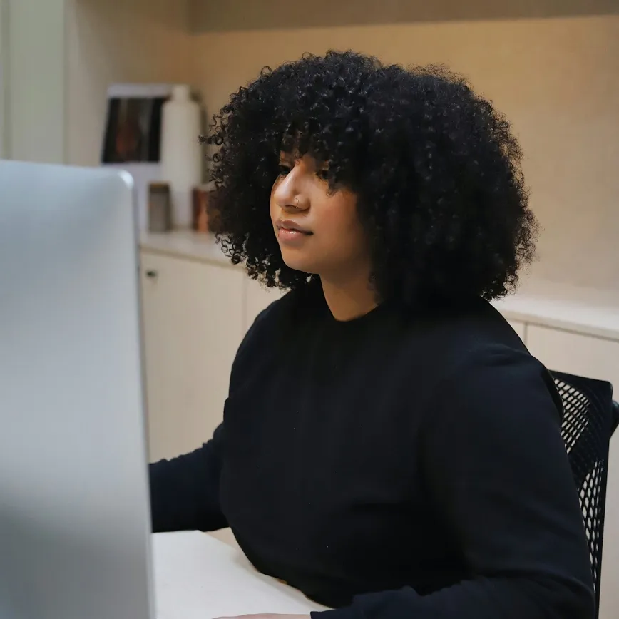 Young woman with curly hair focused on work in front of a desktop computer.