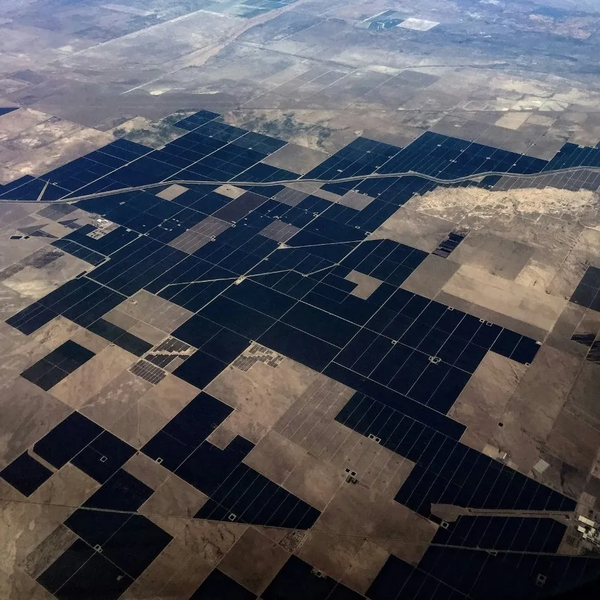 Aerial view of desert farmland with large black irrigation fields segmented by roads and dry land.