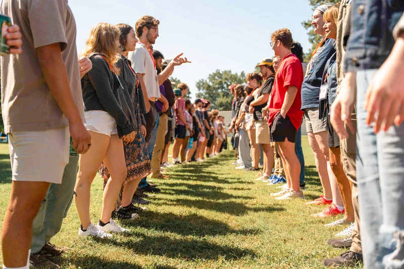 Large group of people standing in two parallel lines facing each other outdoors on grass under a clear sky.