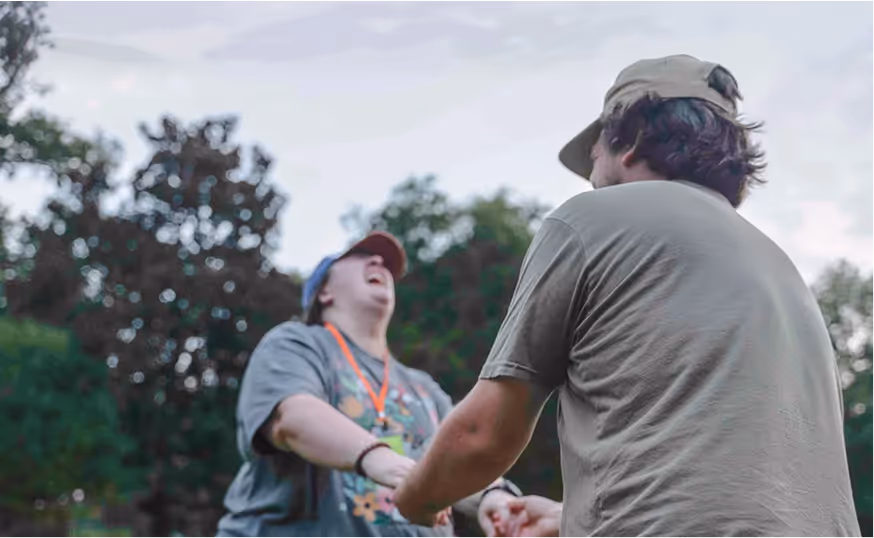 Two people holding hands and laughing outdoors with trees in the background.