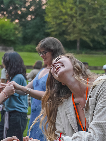 Young woman with long hair laughing joyfully outdoors with other people in the background.