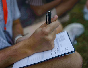 Close-up of a person holding a pen and writing notes on a notepad or form.